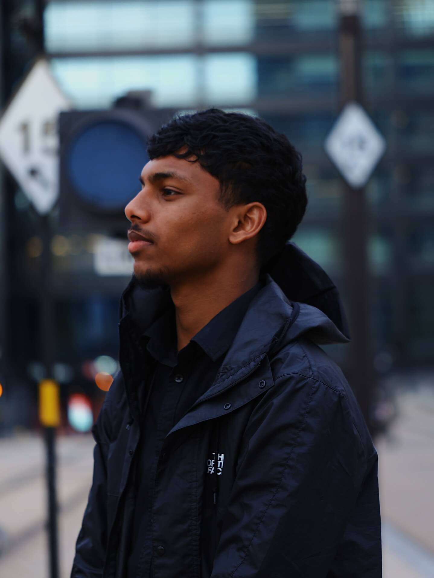 Half body shot of a man wearing a dark jacket standing on a street with blurred background