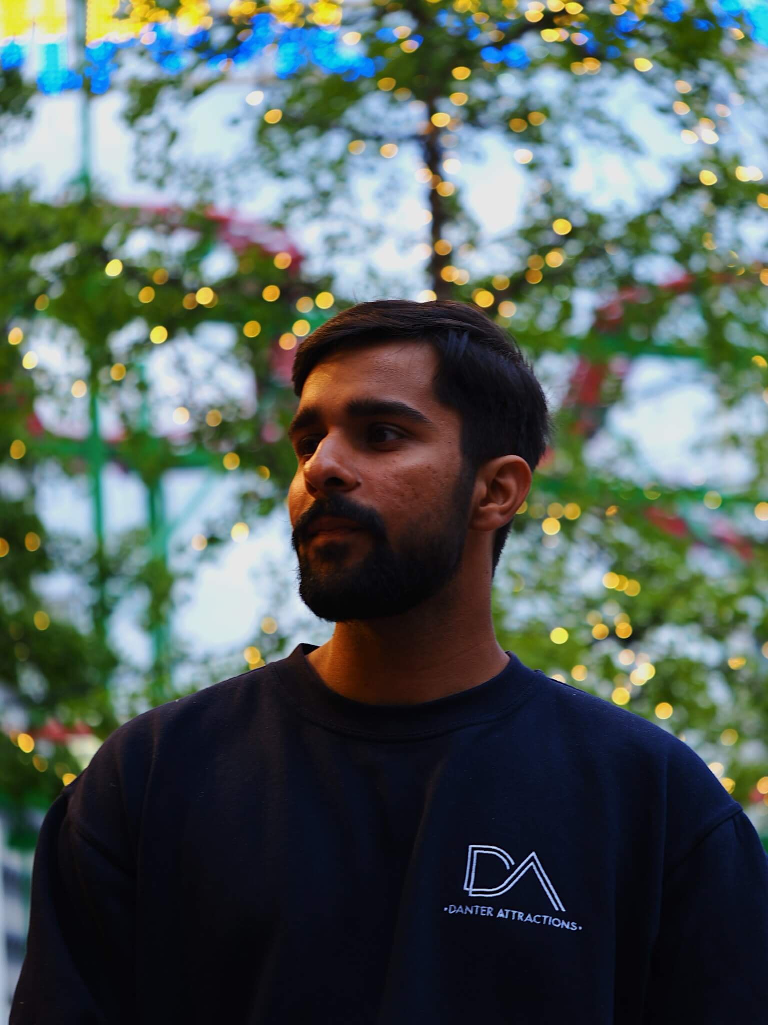 Man wearing a black shirt with a logo in front of a blurred festive background with lights