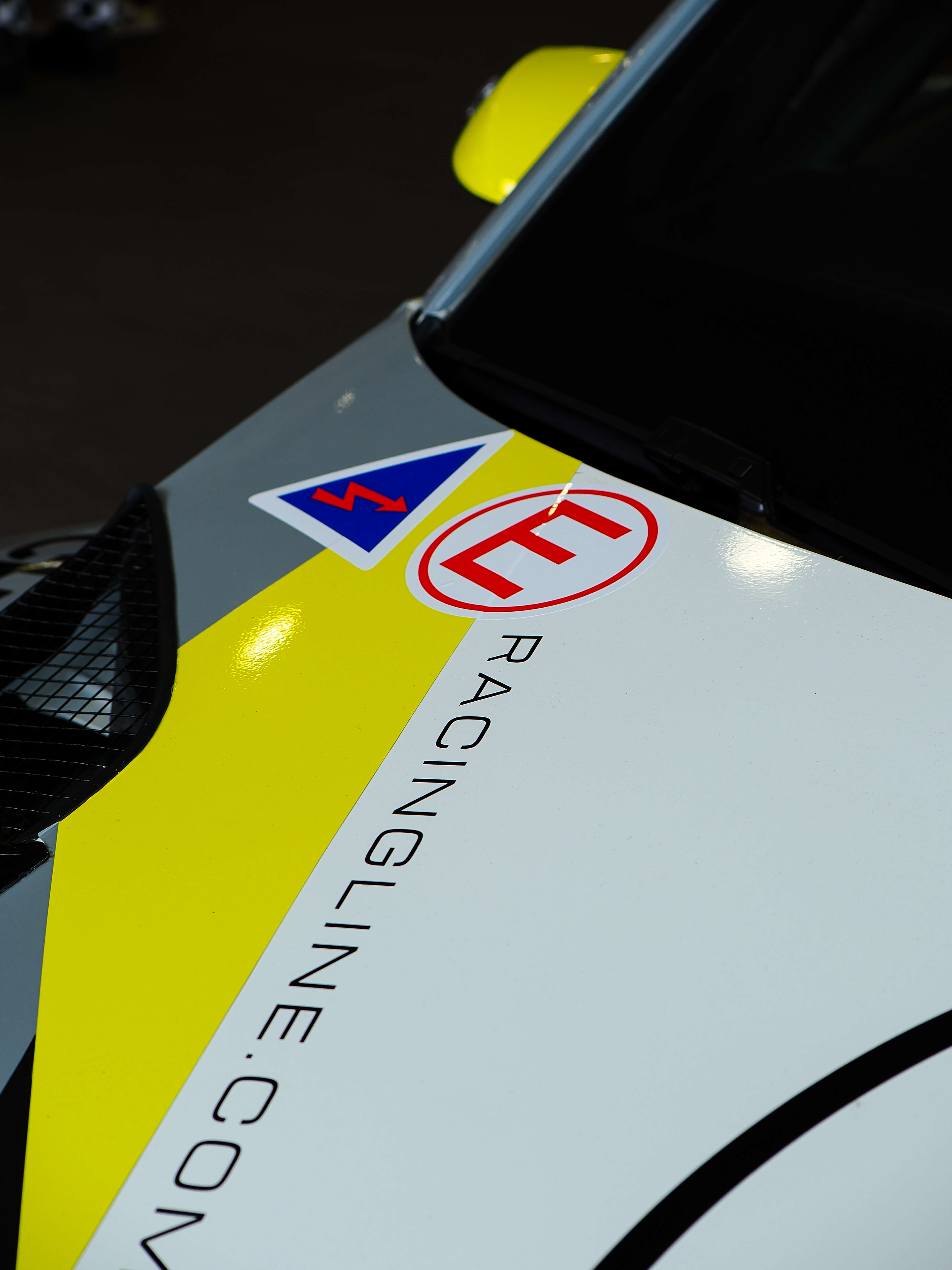 Close-up of a car with racingline.com and logos on a yellow and black background