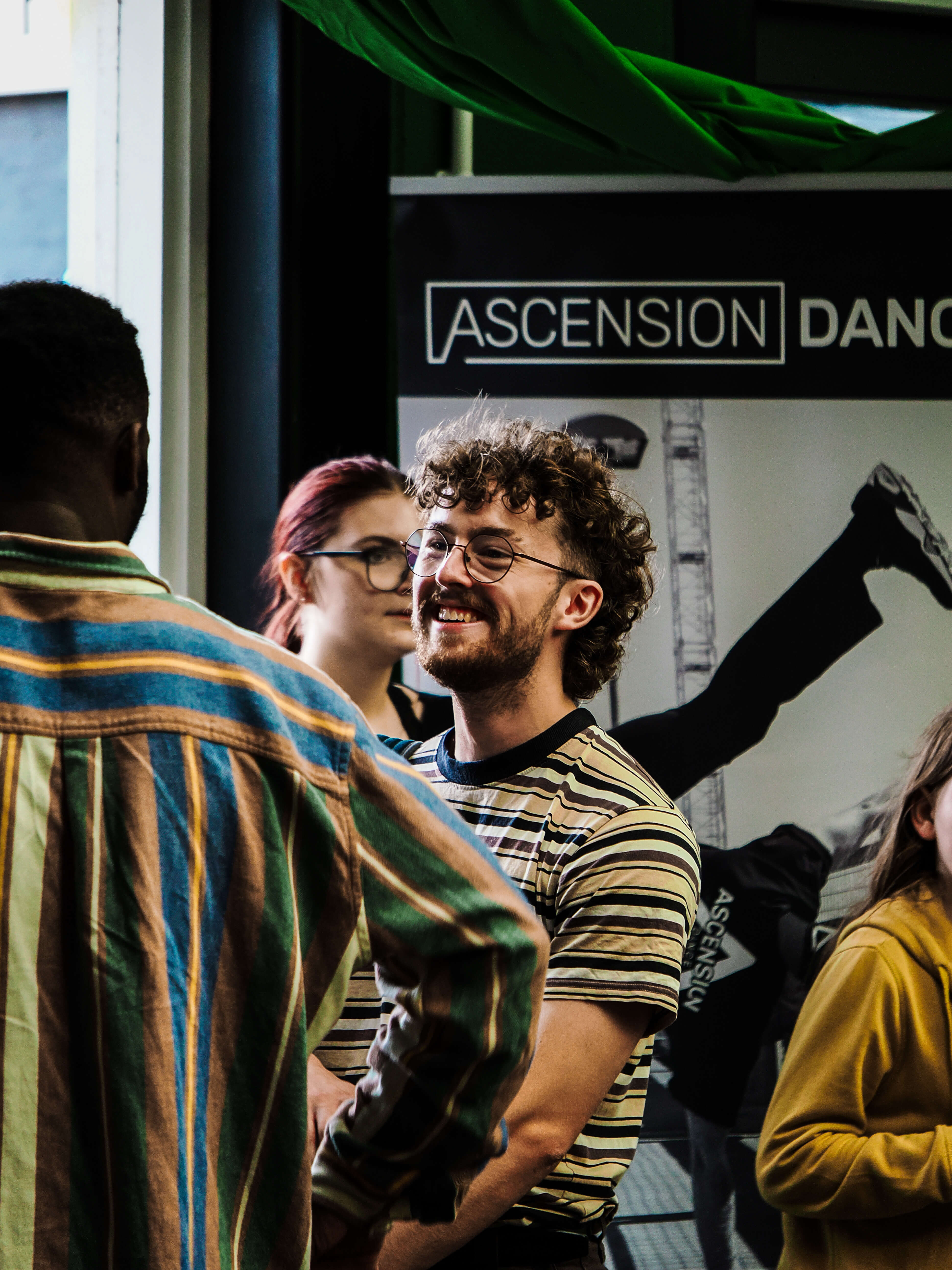 Group of people interacting in a casual setting with 'Ascension Dance' poster in the background