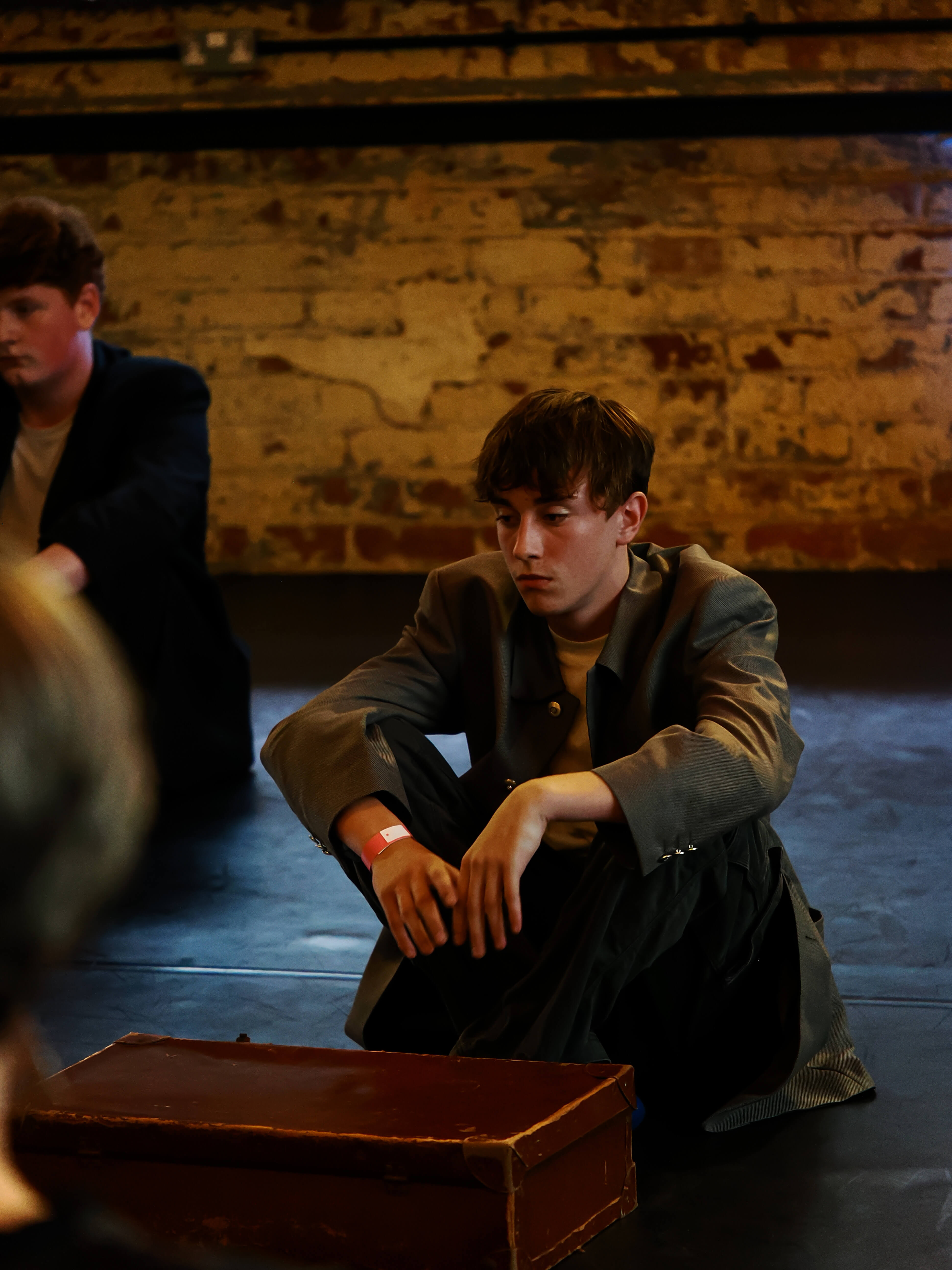 Two individuals at an event sitting on a floor with a brick wall in the background