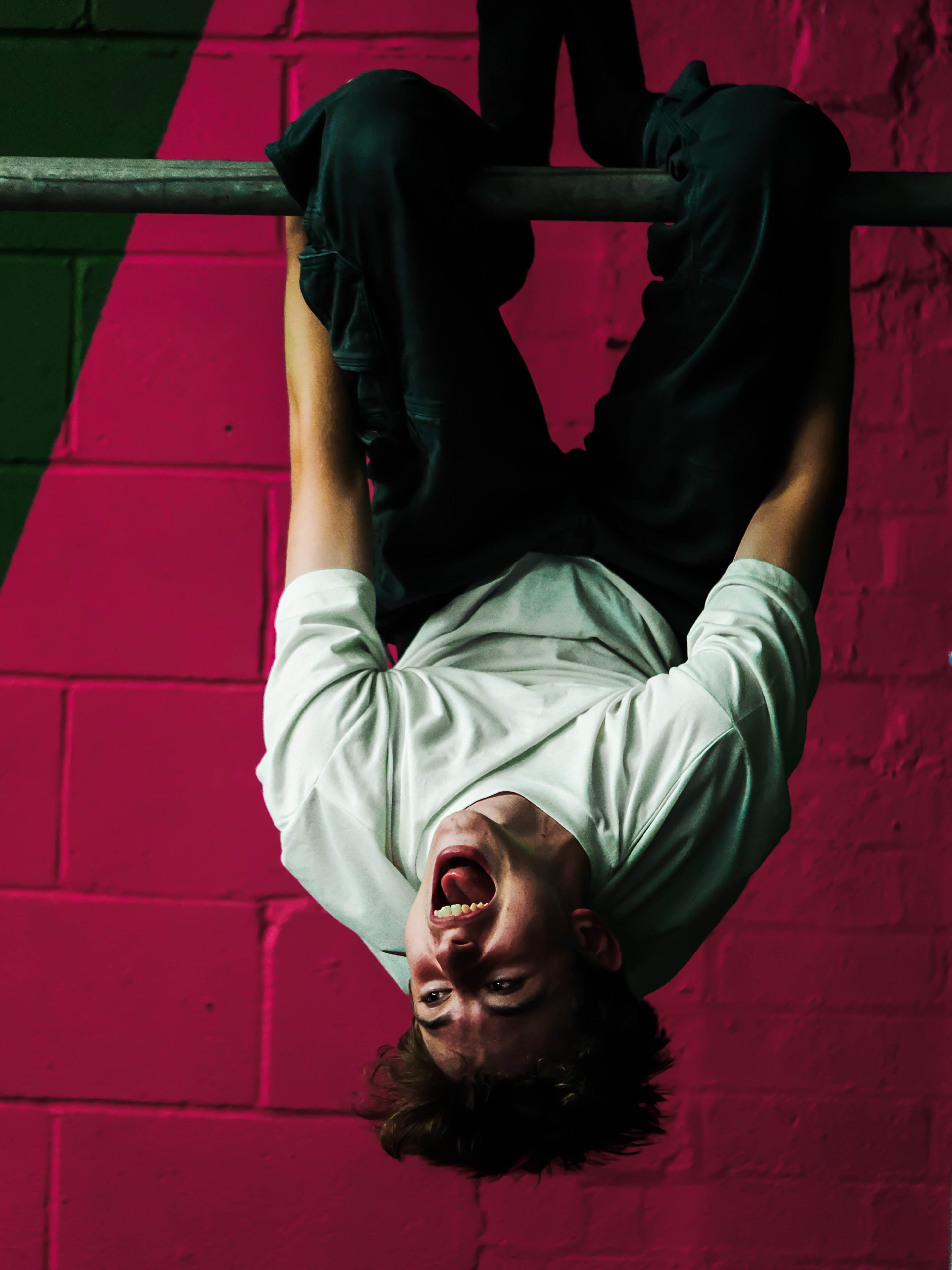 Boy hanging upside down against a pink brick wall at an event
