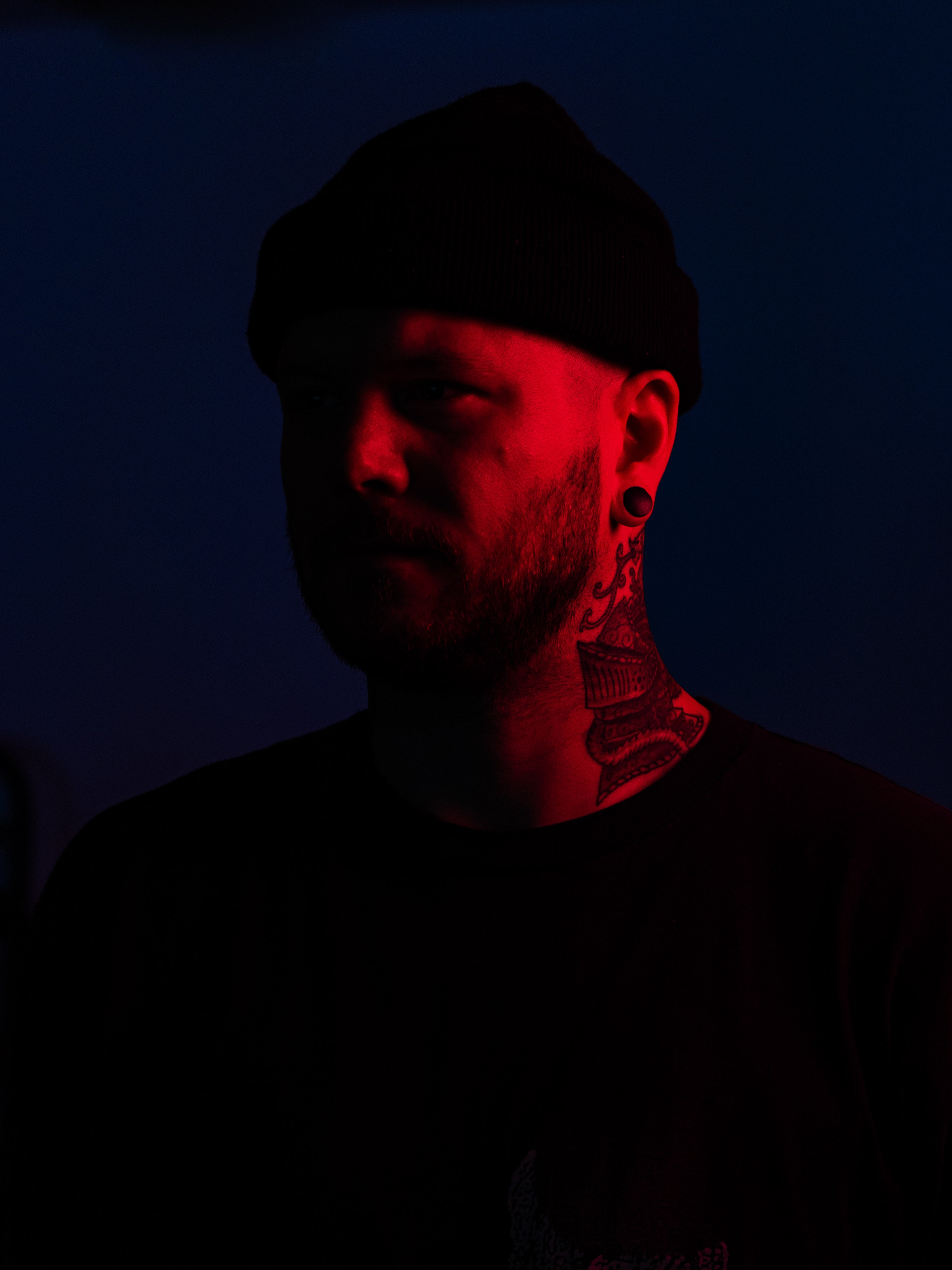 Person with tattoos and a beanie in red light on a dark background