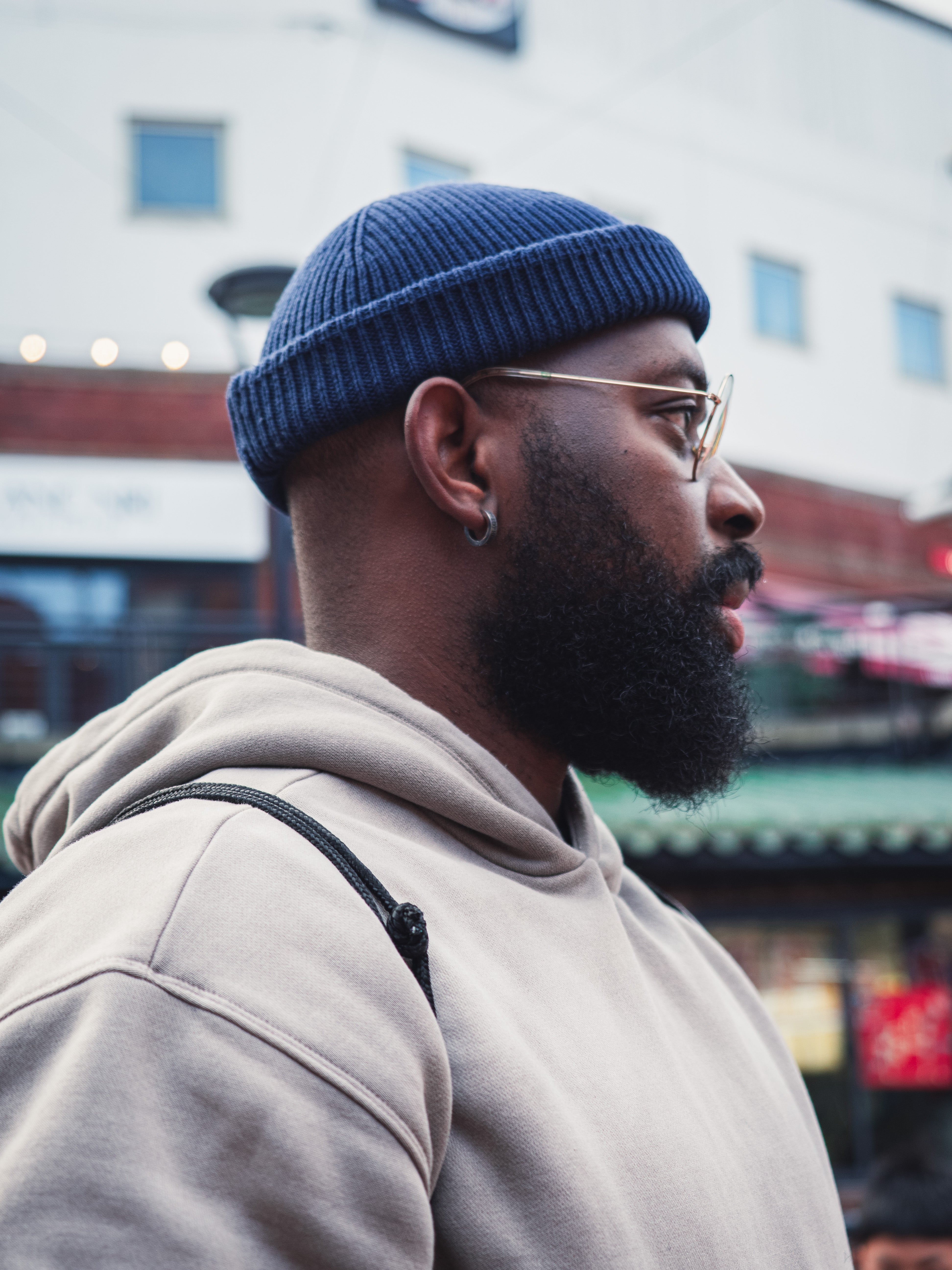 Man wearing a blue beanie and beige hoodie with a blurred background