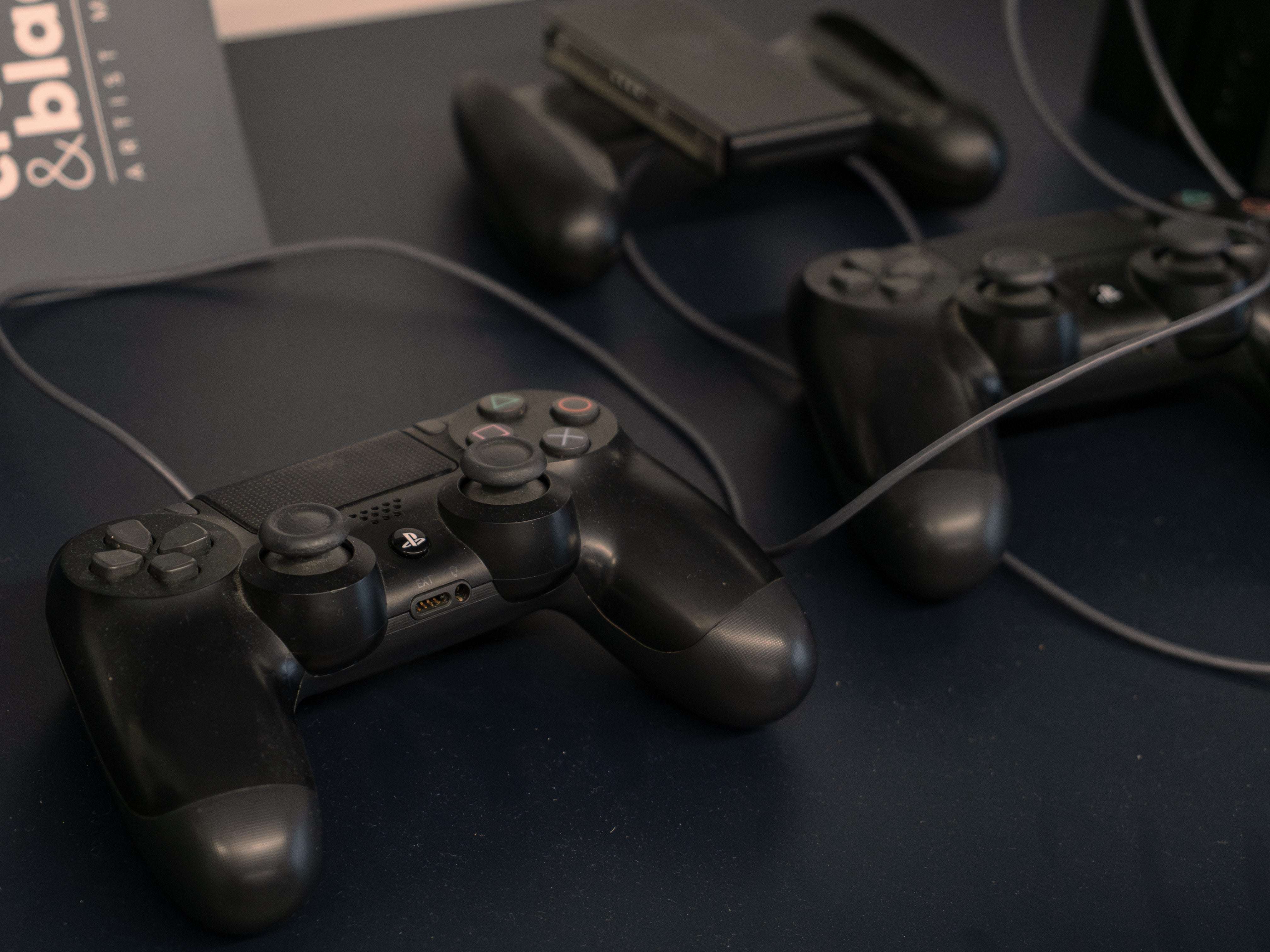 Two black gaming controllers on a dark surface with a blurred background