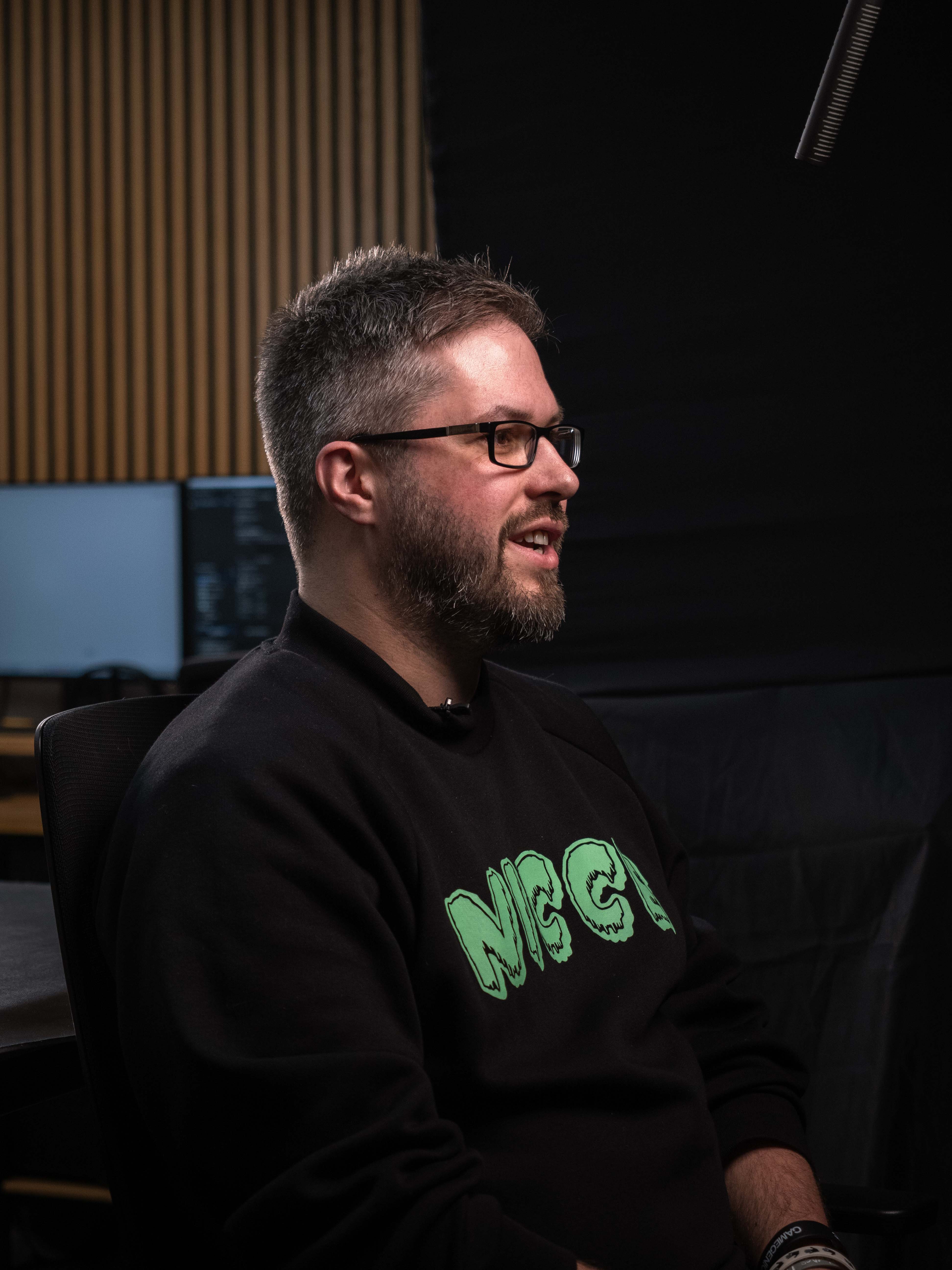 Man wearing glasses and a black sweatshirt with green text in an indoor setting